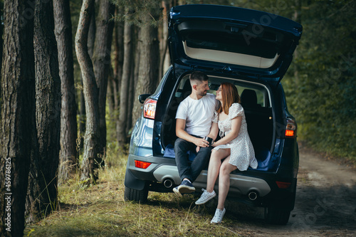 Young couple, man and woman, hugging together on a picnic, sitting in the trunk of a car in the woods, happy together