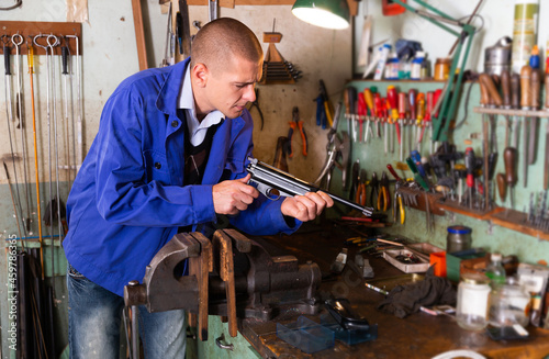 Professional gun repairman performing disassembly of sporting handgun, preparing firearms for preventive maintenance.