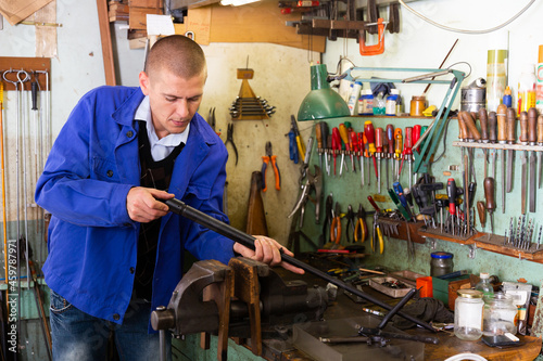 Portrait of professional craftsman engaged in repairing and assembling of shotgun in weapons workshop © JackF