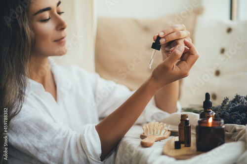 Young woman applying natural organic essential oil on hair and skin. Home spa and beauty rituals.
