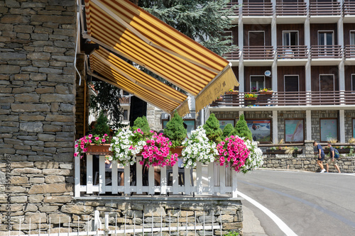 Fototapeta Naklejka Na Ścianę i Meble -  Yellow, striped retractable awning above restaurant with outdoor space for eating with flowers around the fence