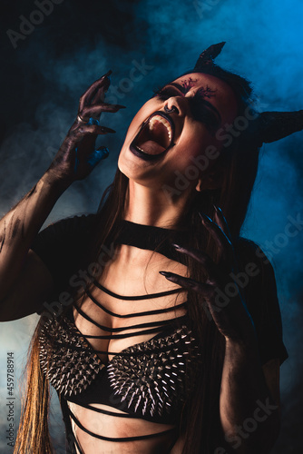 Scary woman halloween portrait demon with horns and emotion with smoke in studio over black background