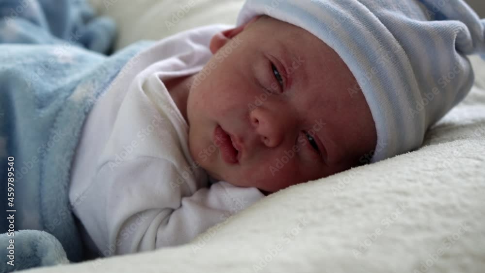 Close-up Newborn Baby Face Portrait Early Days Sleeping Sweetly On Tummy Blue White Background. Child At Start Minutes Of Life on Hat. Infants, Childbirth, First Moments Of Borning, Beginning Concept