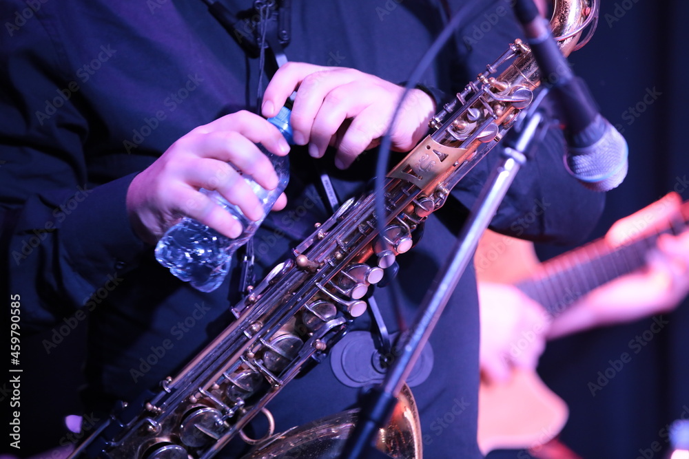 Fototapeta premium Musician playing the saxophone with a bottle of water in his hands during a break in the performance