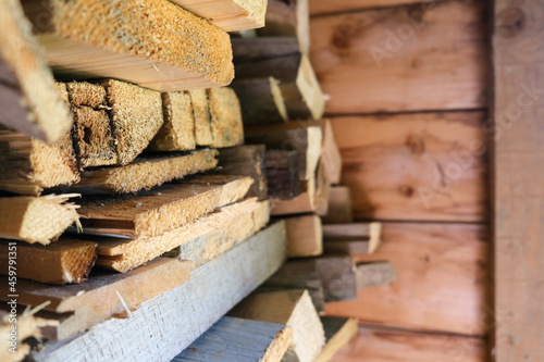 Old sawn pine boards stacked, piled near the wall used as firewood
