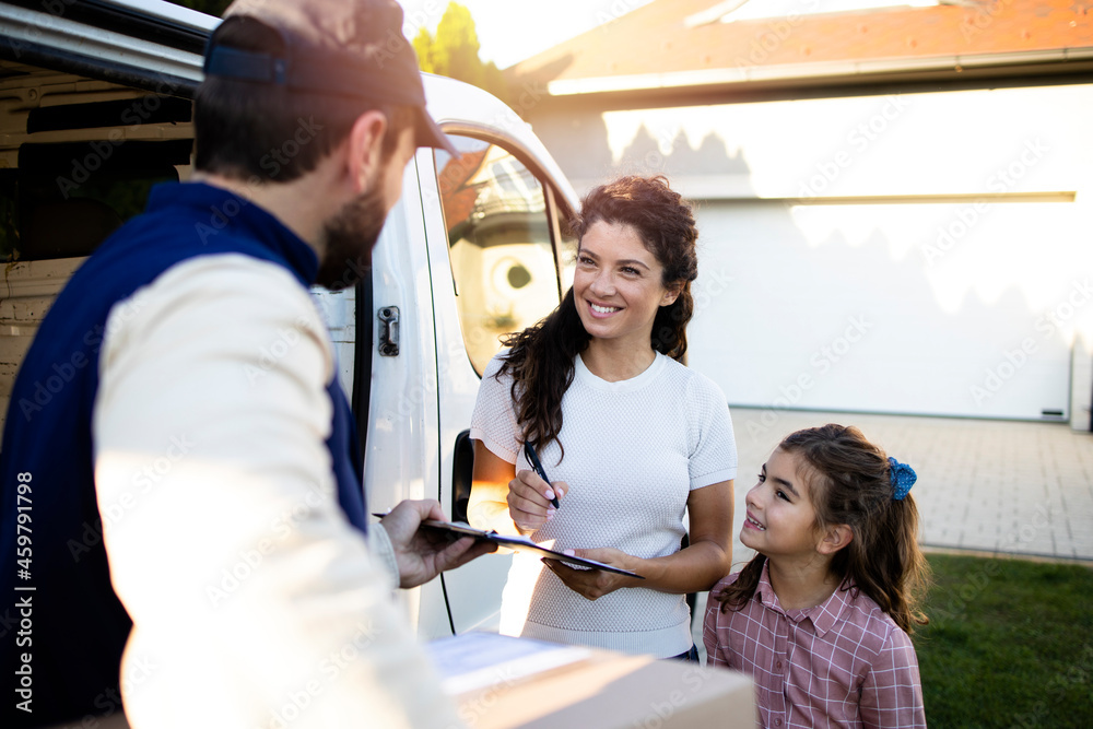 Obraz premium Delivery man delivering parcels to beautiful woman and her daughter in front of the house.