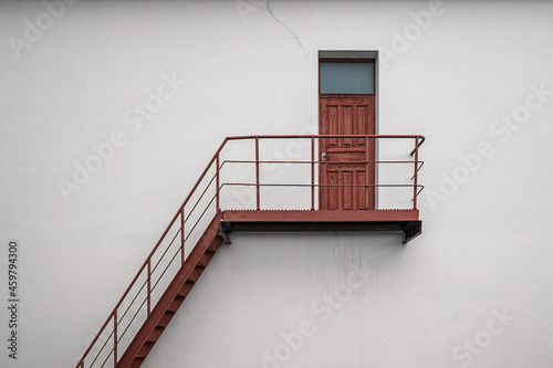 Brown vintage wooden backdoor with metal stair and handrails on white concrete building wall photo