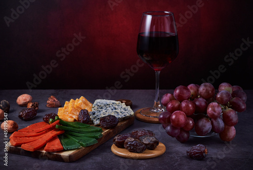 Still life with assorted cheese, red wine in a glass, red grapes and dates.