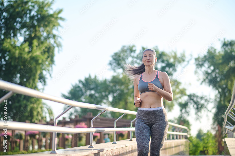 A woman in grey sportswear jogging in the park