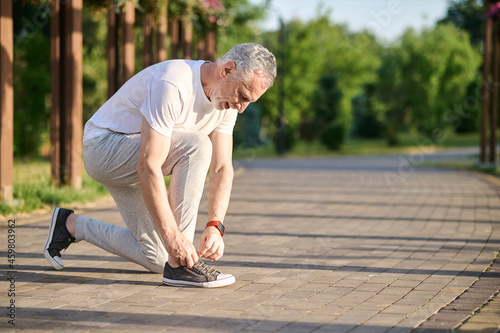 A mid aged man in sportswear lacing his snickers