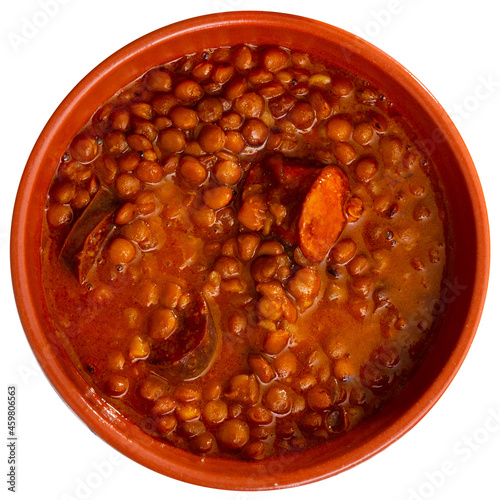 Stewed lentils with chorizo and vegetables with thick tomato sauce served in earthenware bowl. Typical Spanish cuisine. Isolated over white background photo