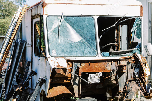 A totaled bus with a shattered windshield and rusty gutted front at a salvage junk yard.  photo