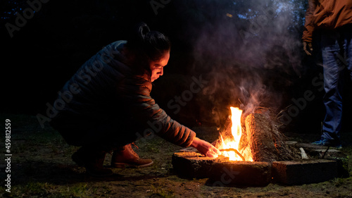 A woman lighting a campfire at night in the forest