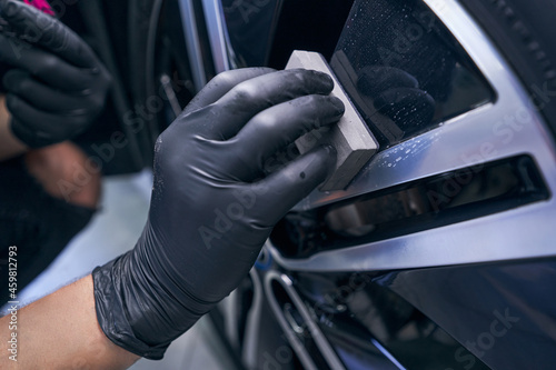 Wax car wheel tire closeup. Service worker perform waxing with sponge