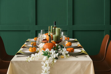 Autumn table setting with fresh pumpkins and flowers near green wall