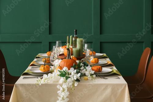 Autumn table setting with fresh pumpkins and flowers near green wall