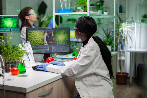 African american doctor researcher typing biochemistry medical expertise analyzing plant with genetic mutation on computer in microbiology hospital laboratory. Genetically modified plants on screen