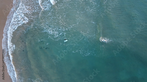 Surfers in the surf waiting for waves in the tuquoise ocean off the Victorian Coastline, top down aerial drone view