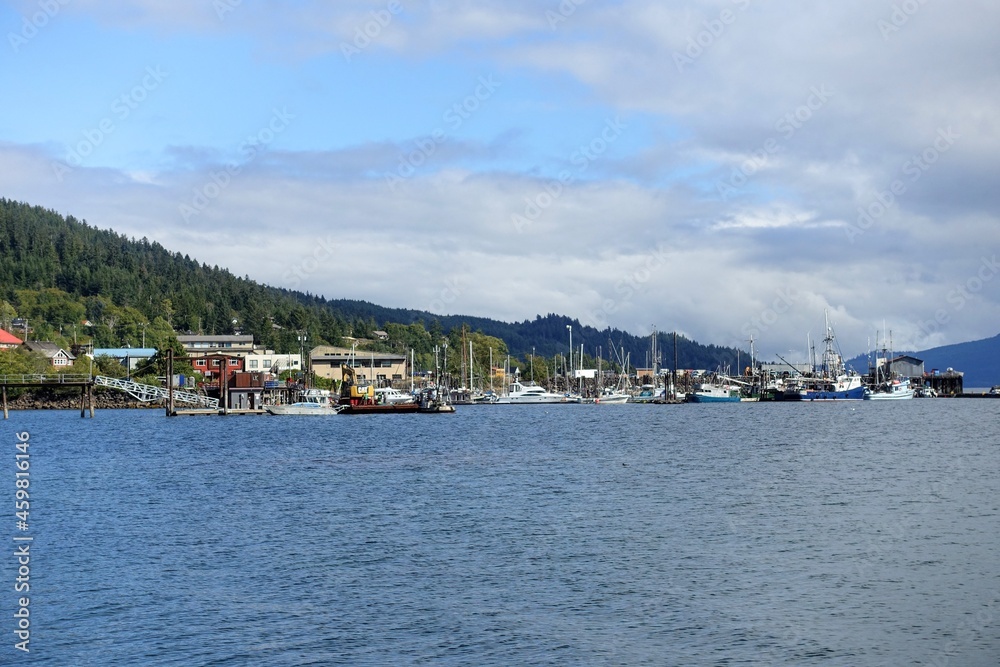 A far away wide view from the ocean looking on land of the port and town of Queen Charlotte, surrounded by forest, in Haida Gwaii, British Columbia, Canada