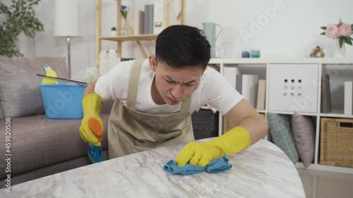 closeup shot of a compulsive Chinese male clean freak holding a spray and rubbing the table with a rag obsessively in the living room at home photo