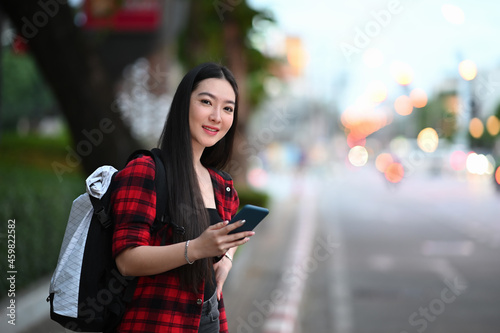 Young woman using application of taxi service app on smart phone while standing on street.