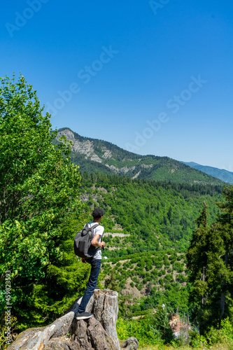 A young man stands on the edge of a cliff overlooking the mountains. Summer hiking in the mountains.