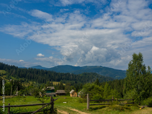 Carpathian landscape with cloudy sky. A wooden house on a green meadow in mountains near old forest. Lifestyle in the Carpathian village. Ecology protection concept. Explore the beauty of the world.