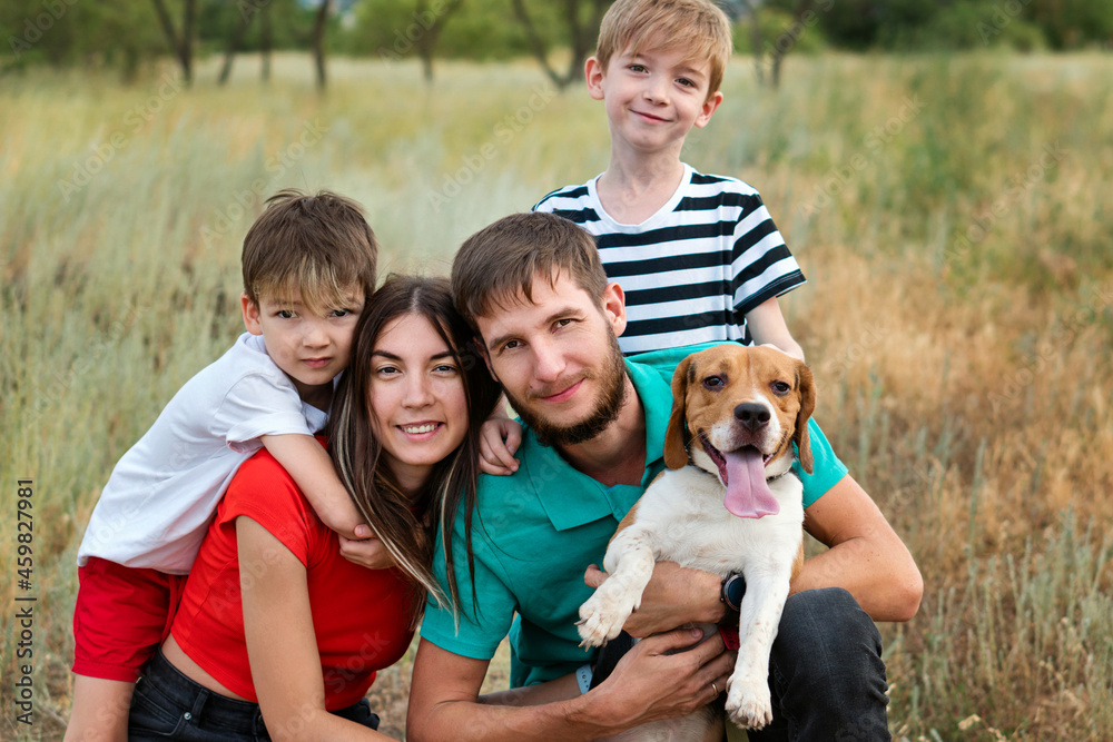 Family of Four Having Fun Playing with Purebred Beagle Dog In Rural Settings. Authentic group people portrait. Animals and friendship. Life in the Countryside Family of Four Having Fun Playing with Purebred Beagle Dog In Rural Settings. Authentic group people portrait. Animals and friendship. Life in the Countryside