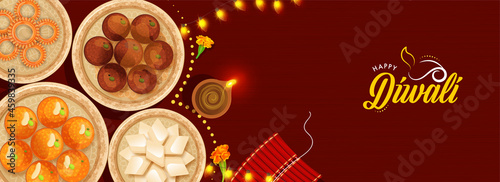 Top View Of Presenting Indian Sweets With Lit Oil Lamp (Diya), Firecracker Stripe And Lighting Garland On Red Background For Happy Diwali Celebration.