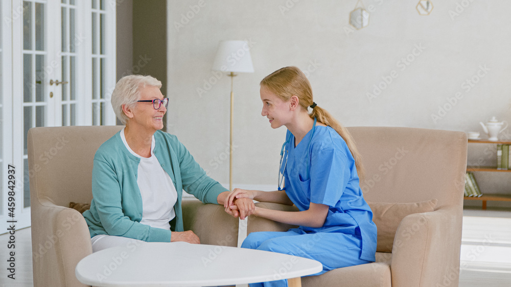 Obraz premium Positive doctor joins hands cheering up mature grey haired lady sitting in armchairs in stylish office
