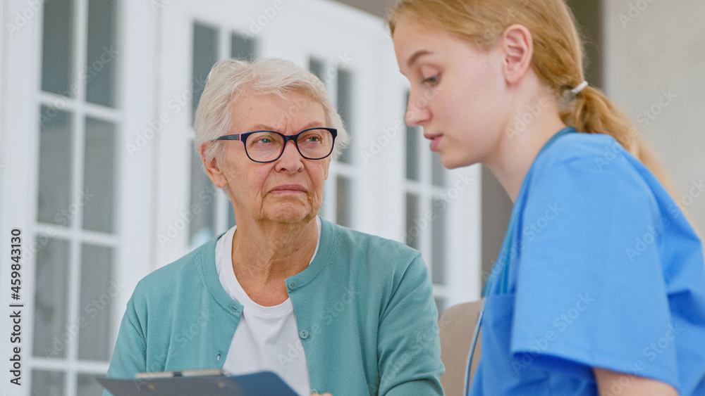 Fototapeta premium Young doctor shows test results on clipboard to doubting senior patient in light office
