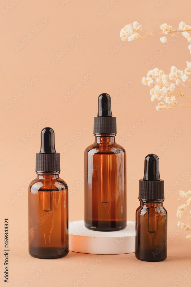 Amber glass dropper bottles different sizes with black lid on white podium for product presentation on beige background with dry plants. Skincare products ,natural cosmetic. Beauty concept for face