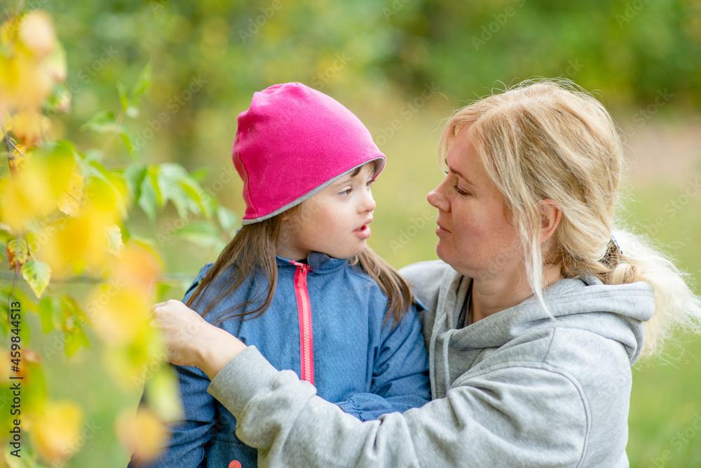 Mother hugs little girl with special needs in autumn park