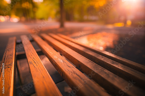 Fall park bench autumn urban landscape recreation. Peaceful relaxing sunset closeup of wooden bench with blurred bokeh forest tress, sun rays. Idyllic seasonal nature concept, dreamy October landscape