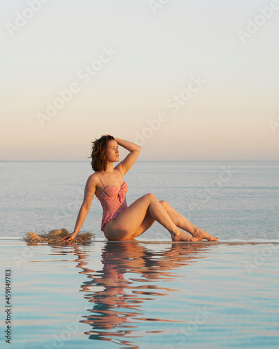 girl in a red and white stripes swimsuit lies on the edge infinity endless pool in Egypt