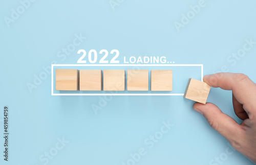 Loading new year 2022 with hand putting wood cube in progress bar. Loading new year 2022 concept. blue background