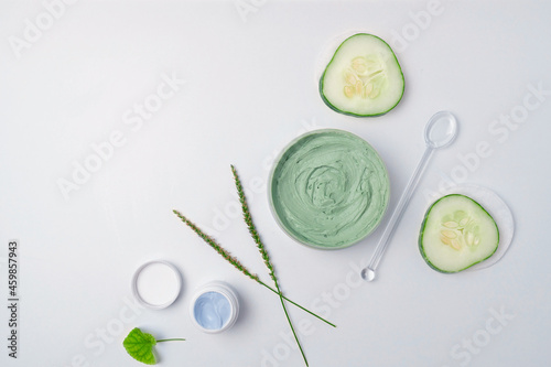 Composition with organic moisturizer cream jar with eco plant leaves, cucumber on white background. Flat lay, top view, copy space. Natural organic products, beauty and SPA concept