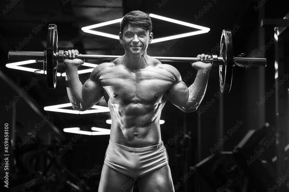 Young athletic man pumping up muscles in the gym at workout. Sport and health care concept background Young athletic man pumping up muscles in the gym at workout. Sport and health care concept background