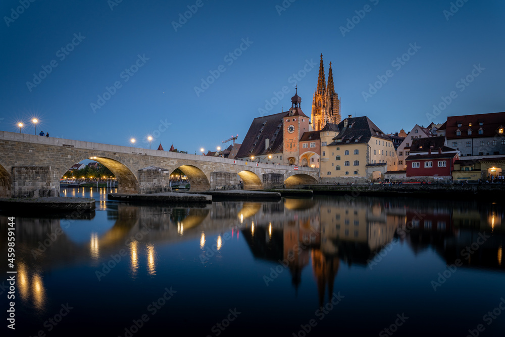 View from the Danube on the Regensburg Cathedral and Stone Bridge with lights in Regensburg in the evening, Germany