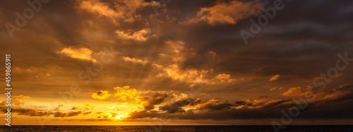 Dramatic golden sunset with sun rays over the sea, horizontally panoramic.