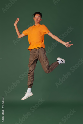 Portrait of young man, student in casual clothes jumping isolated on green vintage studio backgroud. Human emotions concept.