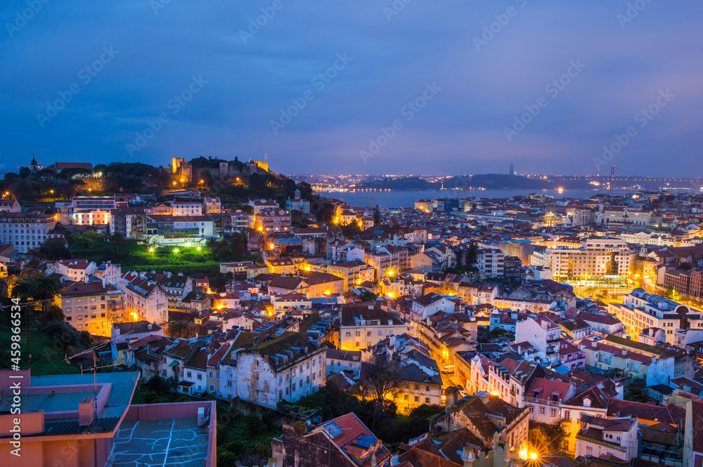 An evening scenic aerial view of the city of Lisbon illuminated by evening lights - the capital of Portugal, located on the hills and washed by the waters of the Atlantic Ocean, the Tagus River.