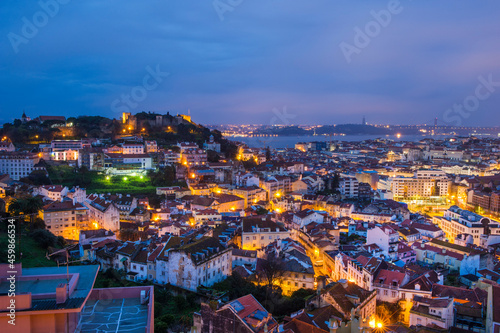 An evening scenic aerial view of the city of Lisbon illuminated by evening lights - the capital of Portugal, located on the hills and washed by the waters of the Atlantic Ocean, the Tagus River. © KSENIYA