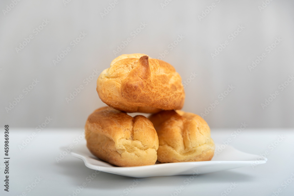Homemade profiteroles or eclairs without cream on saucer. Gray background.