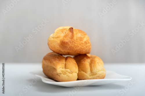 Homemade profiteroles or eclairs without cream on saucer. Gray background.
