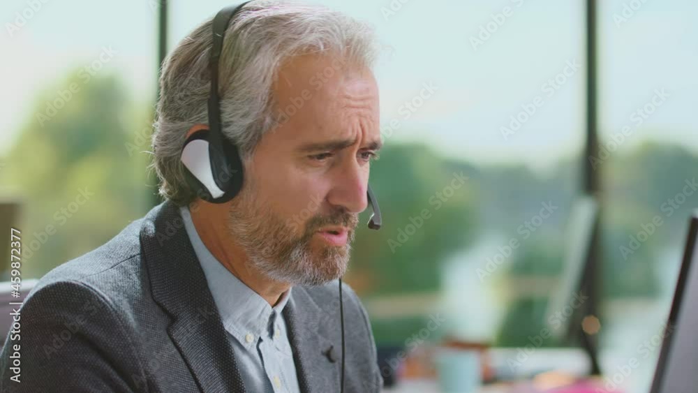 Serious facial expression of experienced businessman while having call with business partner. Modern open space office interior. Serious facial expression of experienced businessman while having call with business partner. Modern open space office interior.