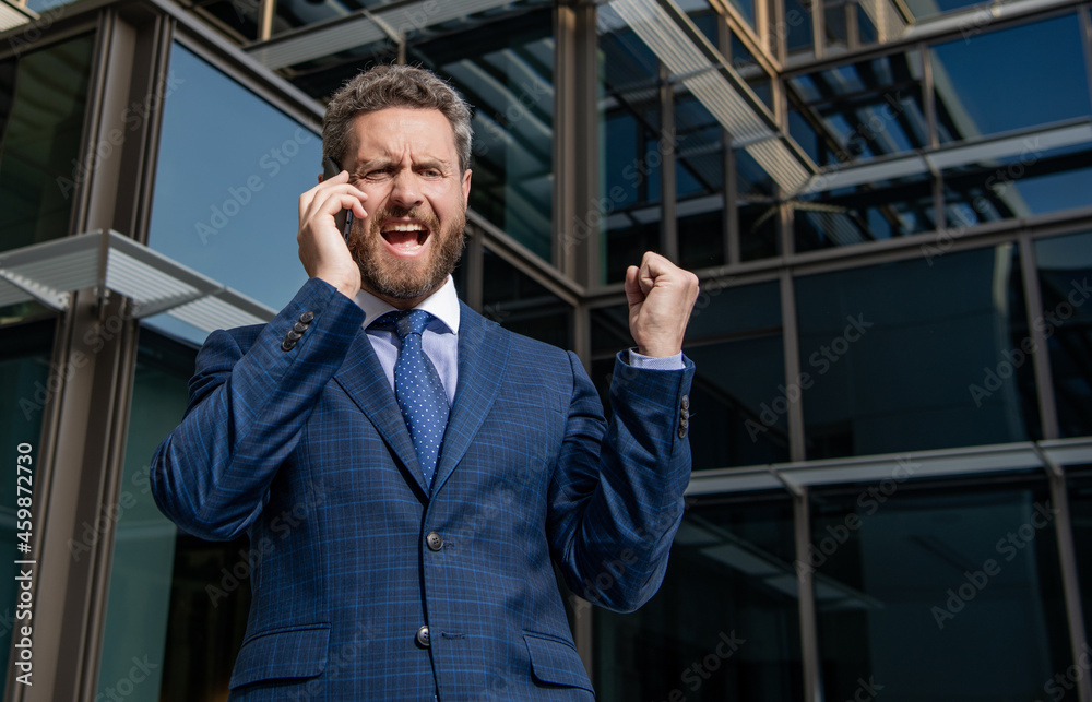 angry entrepreneur in suit shouting while phone conversation outside the office, frustration. angry entrepreneur in suit shouting while phone conversation outside the office, frustration.