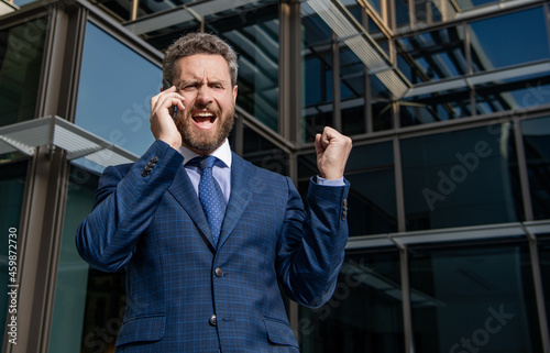 angry entrepreneur in suit shouting while phone conversation outside the office, frustration.