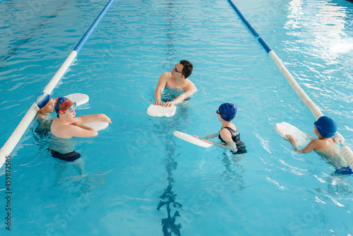 A group of boys and girls train and learn to swim in the pool with an instructor. Development of children's sports.