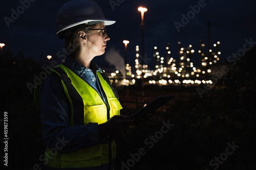 Female engineer wearing hardhat and reflective clothing at factory during night photo